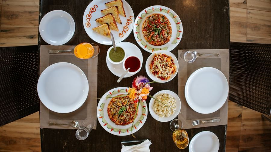 An overhead shot of a dark table set with 6 plates of various Indian snacks and flatbreads, at Daksh Resort & Amusement Park, Sasan Gir.