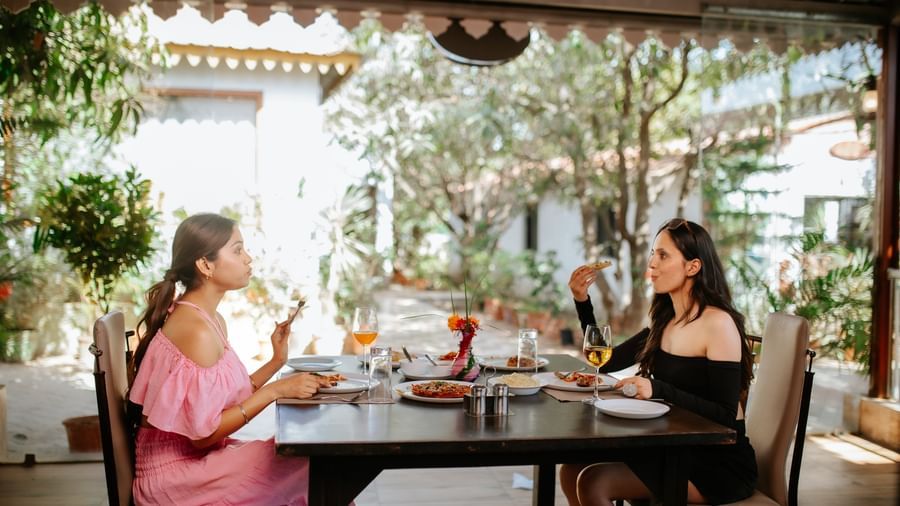 2 women are seated at an outdoor restaurant table having a meal, at Daksh Resort & Amusement Park, Sasan Gir.