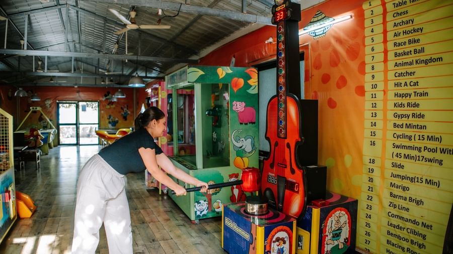 A woman in white plays a boxing arcade game inside the resort's brightly lit games room at Daksh Resort & Amusement Park, Sasan Gir.