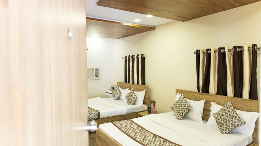 A room with 2 double beds, white and brown bedding and curtains at Daksh Resort & Amusement Park, Sasan Gir.
