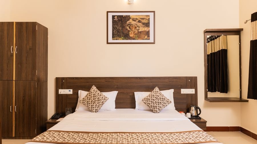 A view of the bed with brown accents, a wall art, a mirror reflecting the curtains, and a wooden wardrobe at Daksh Resort & Amusement Park, Sasan Gir.