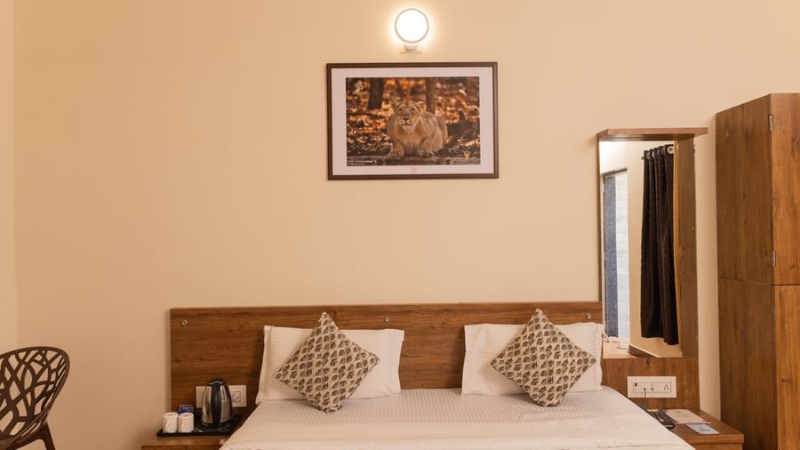 A close-up of a bed with brown accents, a wall art, a wall mirror, and a wooden wardrobe at Daksh Resort & Amusement Park, Sasan Gir.
