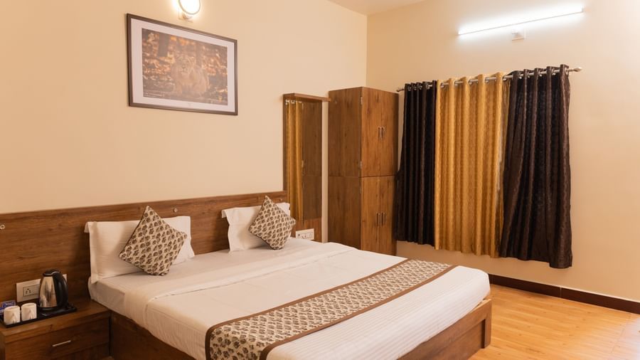 A neatly arranged double bed with patterned cushions and curtains at Daksh Resort & Amusement Park, Sasan Gir.