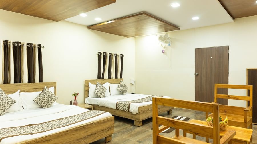 A spacious room featuring a a double beds and a small bed, with light wood furniture, at Daksh Resort & Amusement Park, Sasan Gir.