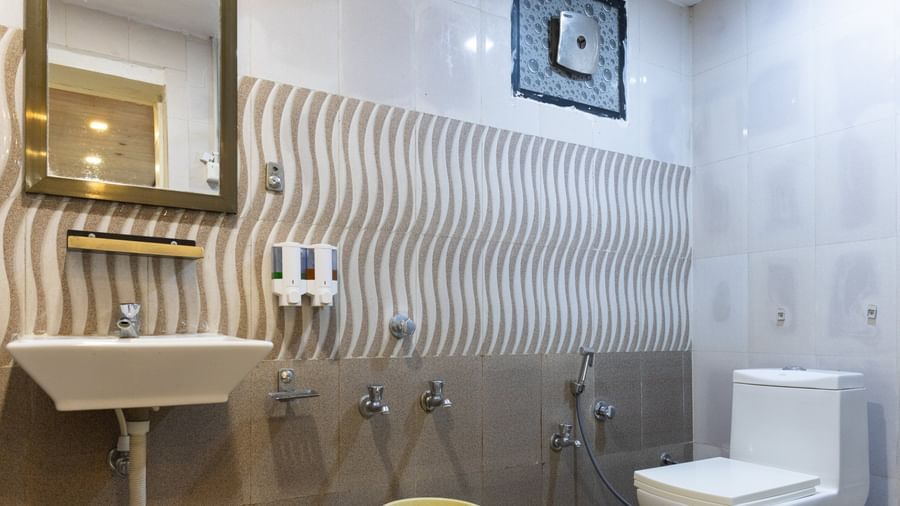 A modern bathroom with brown wave-textured tiles, a square mirror, a sink, and a toilet, at Daksh Resort & Amusement Park, Sasan Gir.
