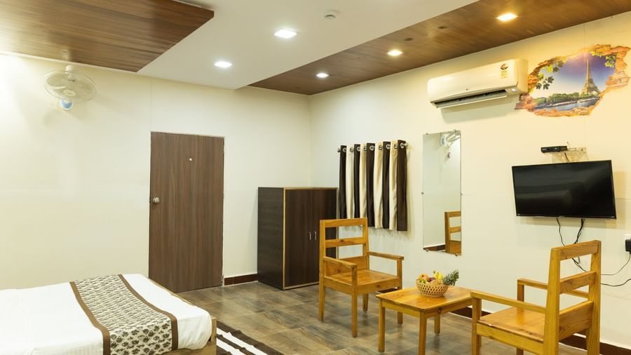 A wide view of a room featuring 2 beds, a TV, wooden chairs and a table, and wooden safe, at Daksh Resort & Amusement Park, Sasan Gir.