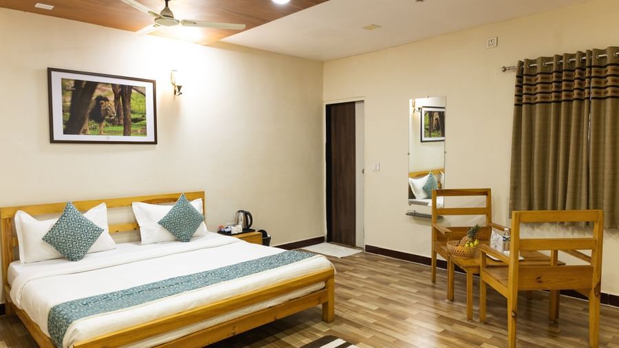 A room with a large bed, blue accents, a striped runner rug, a wall art, and wooden furniture, at Daksh Resort & Amusement Park, Sasan Gir.