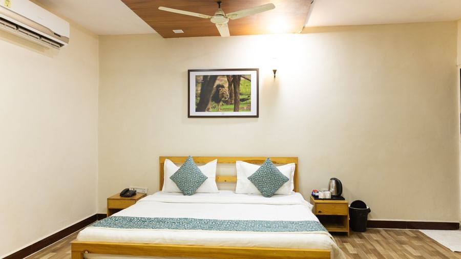A clean room with a king size bed, blue accents, bedside table, and a picture on the wall, at Daksh Resort & Amusement Park, Sasan Gir.