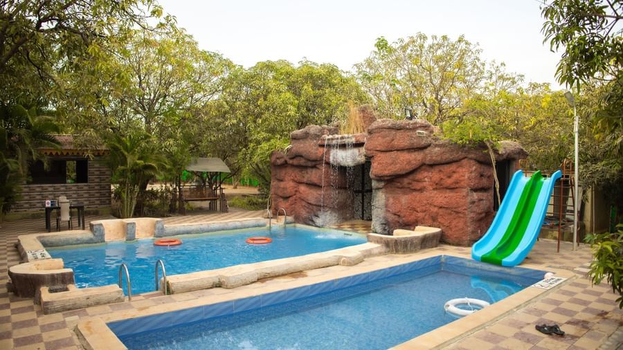 2 swimming pool featuring slides and an artificial waterfall surrounded by greenery at Daksh Resort & Amusement Park, Sasan Gir.