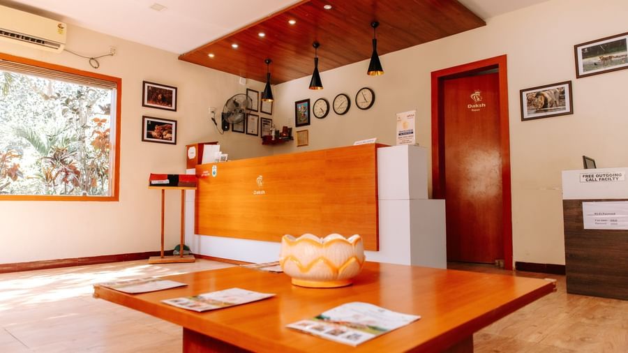 A warmly lit indoor reception area with a wooden desk and wall arts at Daksh Resort and Amusement Park.