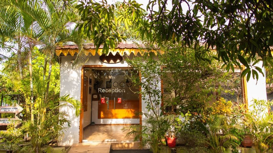 A lush green entrance to a stone-walled cottage framed with potted plants at Daksh Resort and Amusement Park.
