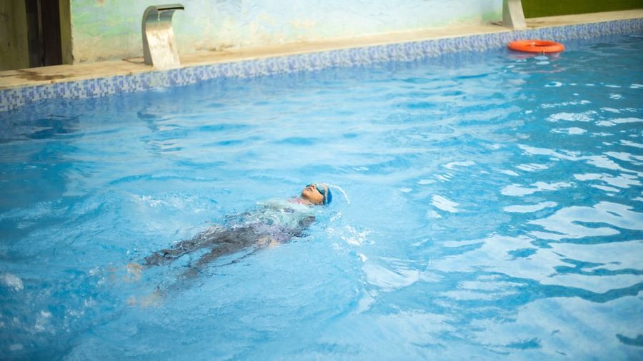 A guest swimming in a blue-tiled pool with safety rings nearby at Daksh Resort and Amusement Park.