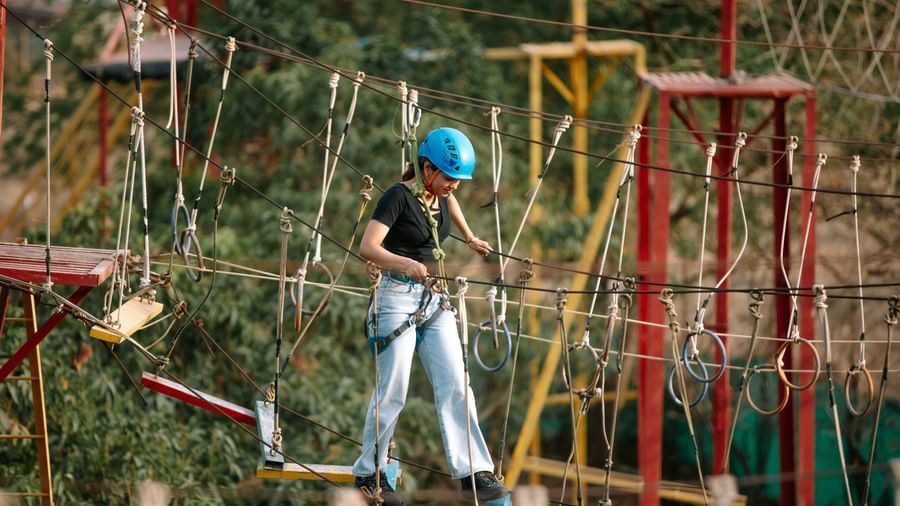 A child navigating a rope obstacle course wearing safety gear at Daksh Resort & Amusement Park.