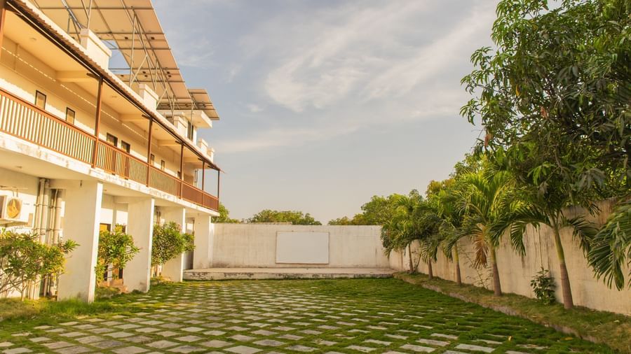 Exterior of a resort building with balconies and patterned yard flanked by greenery on the side at Daksh Resort & Amusement Park.