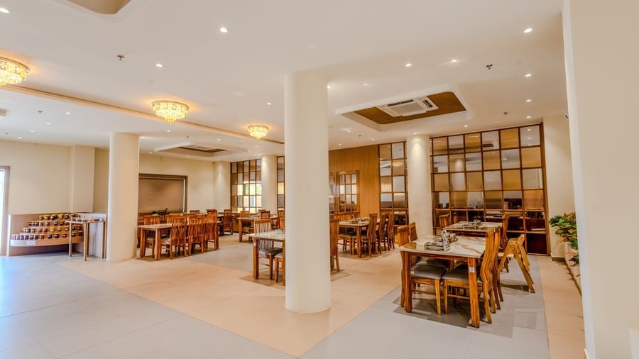 Full-view shot of the restaurant at Daksh The Grand Goverdhan, Dwarka, featuring 4 white-coloured cylindrical pillars supporting the ceiling.