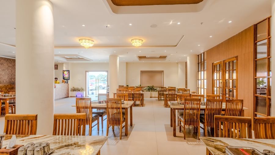 A wide-angle shot of the restaurant at Daksh The Grand Goverdhan, Dwarka, with a cosy ambience and plenty of lighting. 