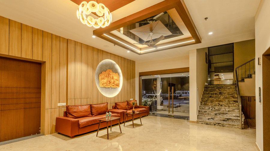 A wide angle shot of an inviting lobby area at Daksh The Grand Goverdhan, Dwarka, with plush seating, elegant decor, and a view of the outside.