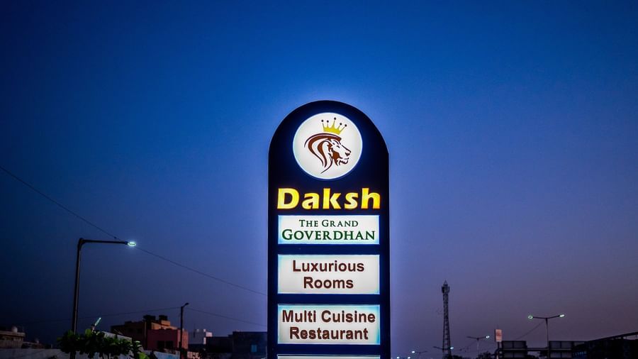 An illuminated signpost in the exterior of Daksh The Grand Gowardhan, Dwarka at dusk, listing out property facilities.