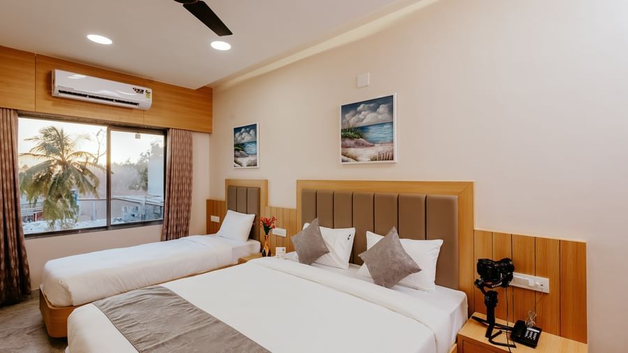 Corner view of a spacious Pride Room at Daksh The Grand Gowardhan, Dwarka, with multiple beds, modern decor, and a window with views.