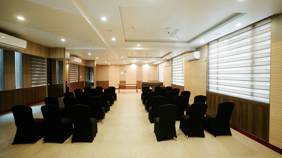Wide angle view of a long, modern conference or banquet hall with rows of black covered chairs set up for a presentation at Daksh The Madhuvan Suites, Dwarka.