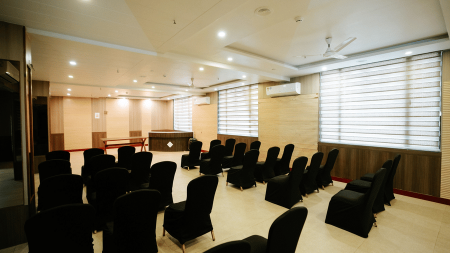Closer view of the rows of black upholstered chairs in the event space, showing the light wood floors and curtained windows at Daksh The Madhuvan Suites, Dwarka.