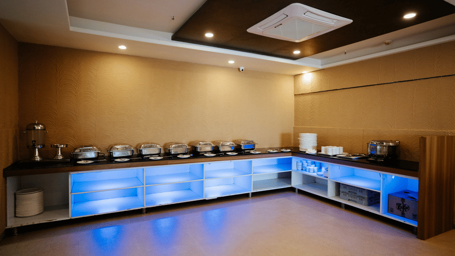 Panoramic view of the long, narrow restaurant hall with set tables and decorative elements on the far walls at Daksh The Madhuvan Suites, Dwarka.