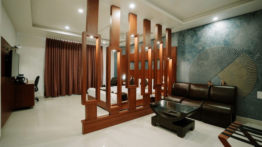 Wide view of a sitting area separated from the bedroom by a stylish, tall wooden slat partition. Dark leather sofa at Daksh The Madhuvan Suites, Dwarka.