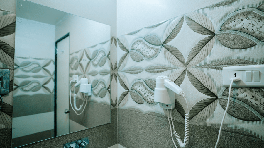 Close-up of the walk-in shower area with a hand-held shower, and a large wall mirror reflecting the patterned tiles at Daksh The Madhuvan Suites, Dwarka.