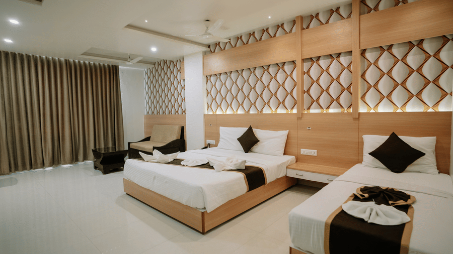 Spacious hotel room with two double beds and a stylish, geometric wooden feature wall above the beds at Daksh The Madhuvan Suites, Dwarka.