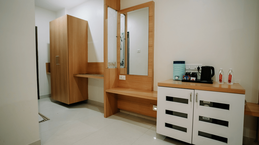Wooden dresser/console with a large mirror, storage drawers, a kettle, and a closet in the hotel room at Daksh The Madhuvan Suites, Dwarka.