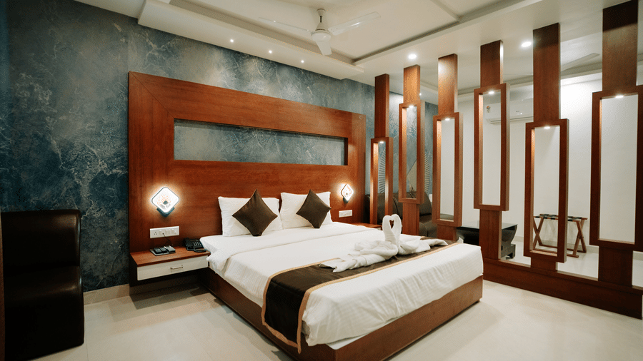 Double bed with dark wood frame and headboard, set against a blue textured feature wall, with decorative wooden partitions at Daksh The Madhuvan Suites, Dwarka.