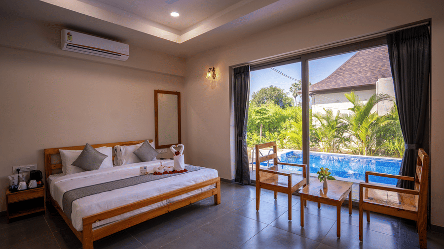 A premium guest room layout showing a decorated bed and direct visual access to the outdoor pool area - Daksh The Nirvana Retreat, Pavagadh