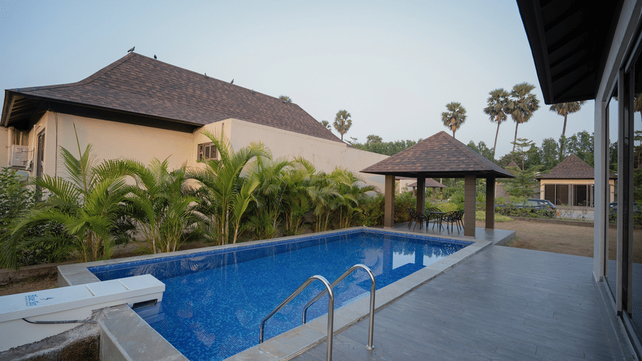 A wide-angle view of a sparkling blue swimming pool located right outside a modern white villa with a dark roof - Daksh The Nirvana Retreat, Pavagadh