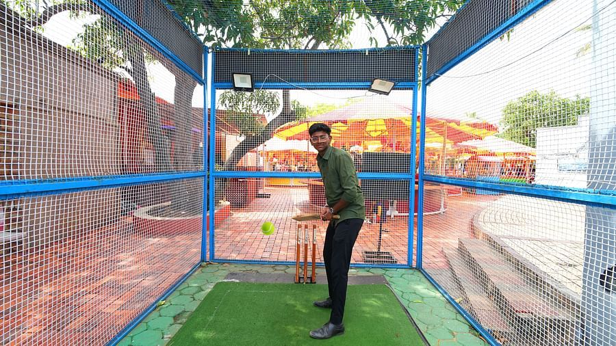 A boy playing cricket in outdoor setting which is covered with nets to prevent cricket ball from going far. 