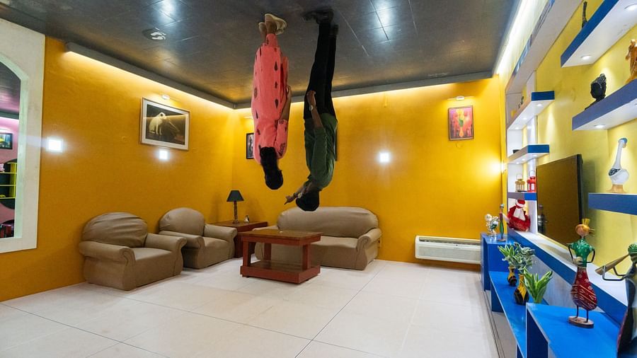 Upside Side Down room at MGM Dizzee World showcasing two people standing on a roof upside down while the other belongings like sofa and cabinets are on the ground placed upright.