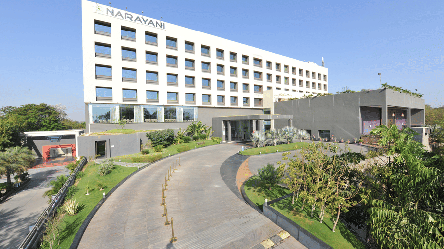 LOng-shot of the facade of Narayani Heights Hotel & Resorts, Ahmedabad with the view of the road leading to the entrance.