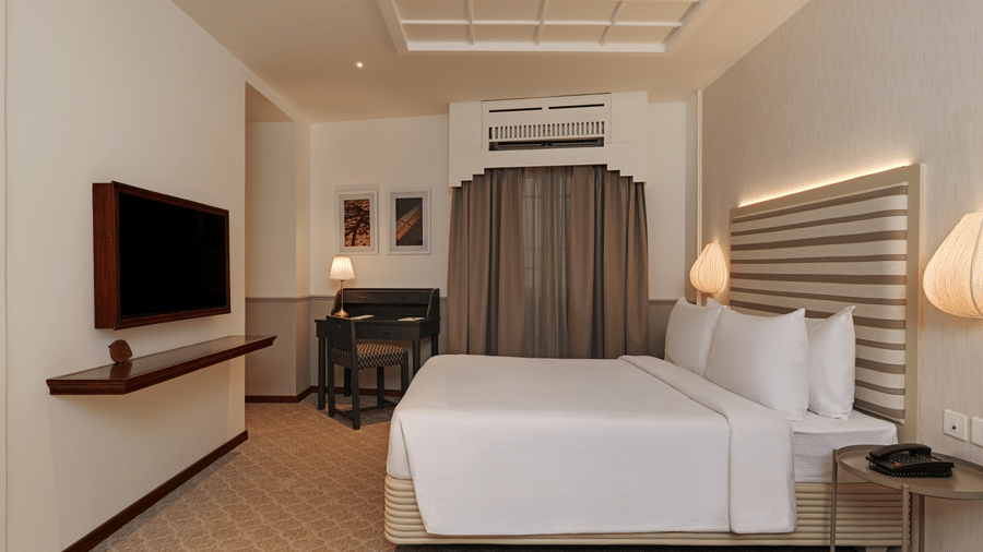 Executive Queen Room at Shilton Suites, Bengaluru, featuring a king size bed, wall mounted television, bedside table, work desk, sofa seating and large wardrobe.