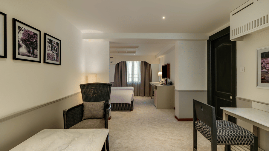 Executive Twin Room at Shilton Suites, Bengaluru, featuring twin beds, bedside tables, upholstered chairs, work desk and large mirror.
