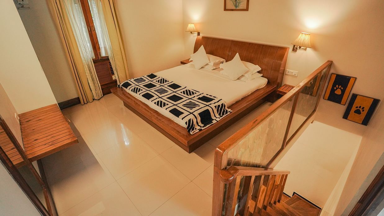 A bedroom with a bed, a chair, and a patterned rug, warm lighting - The Den Corbett Resort & Spa, Kumeria.