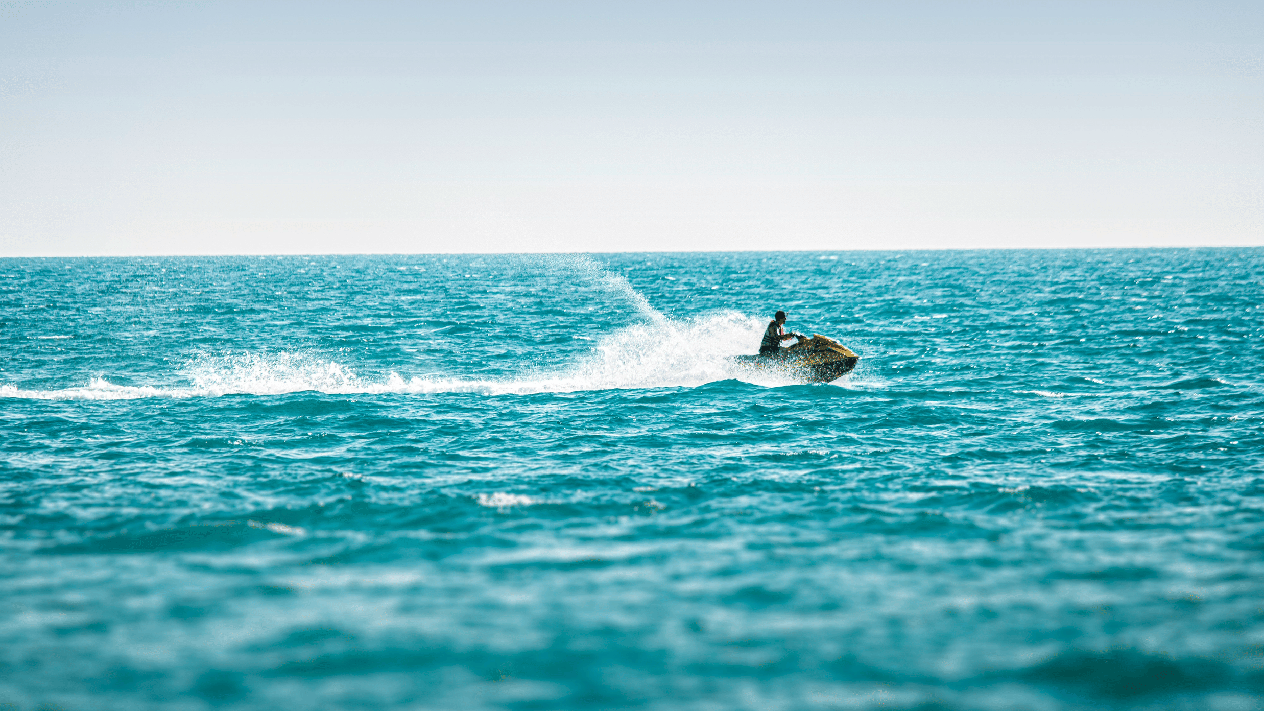 Tourist enjoying a jet ski, creating a trail of water spray against the coastal horizon.