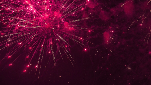 a close up shot of pink coloured fireworks lighting up the night sky 