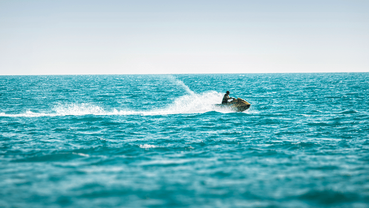 Tourist enjoying a jet ski, creating a trail of water spray against the coastal horizon.