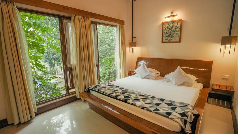 A bedroom with a bed, lamps, and a view of a garden - The Den Corbett Resort & Spa, Kumeria.
