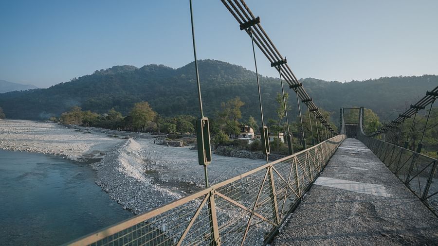 A suspension bridge over a river, with mountains in the background, daytime setting.