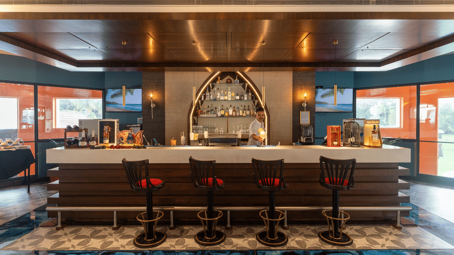 Wooden bar counter with tall stools and an arched shelf at Kenilworth Resort & Spa, Goa.