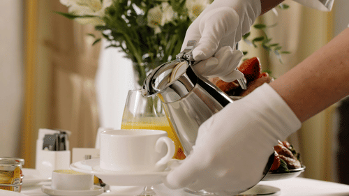 A person pouring coffee into a cup with flowers in the background.