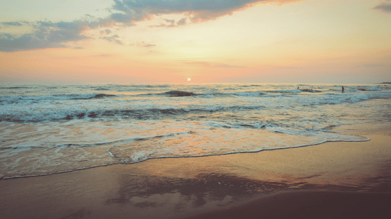 An overview of a beach with the sun setting in the background and different hues on the sky.