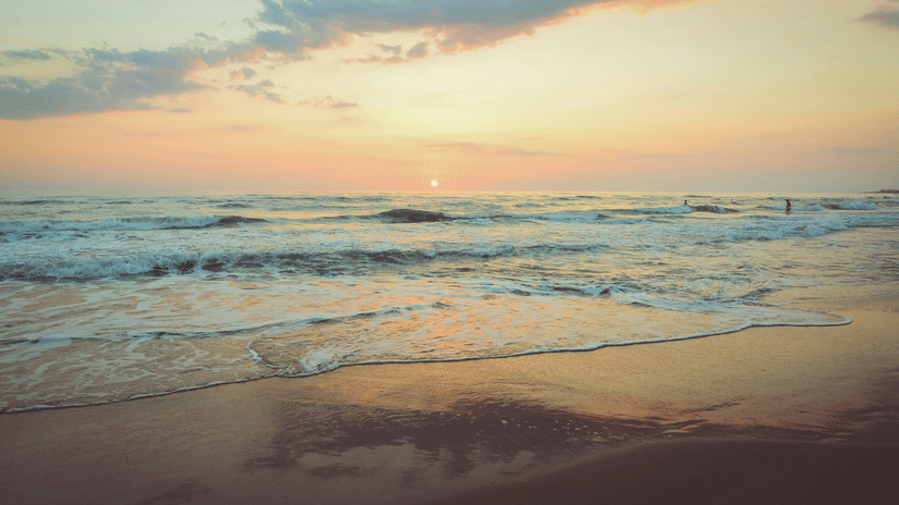 Seaside view of a sandy beach at sunset with gentle waves washing ashore.