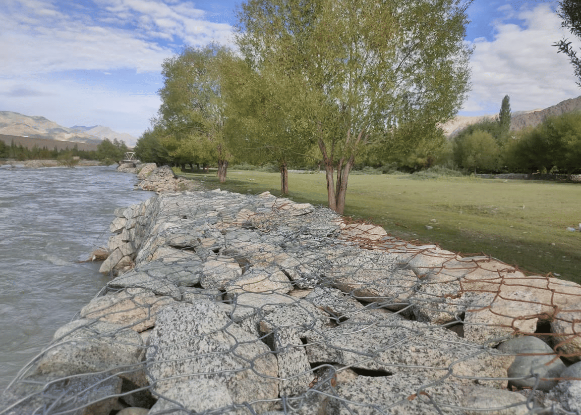 A sturdy stone-paved embankment running alongside a wide, fast-flowing river at Indus Serenity Retreat.