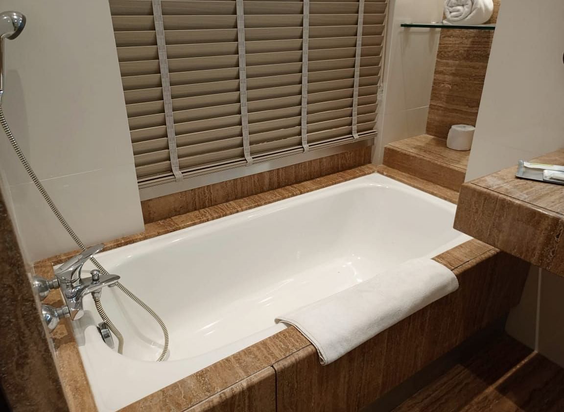 A modern bathroom in an executive room at Mirage Hotel, featuring a white, built-in bathtub, and a wall-mounted hand shower.